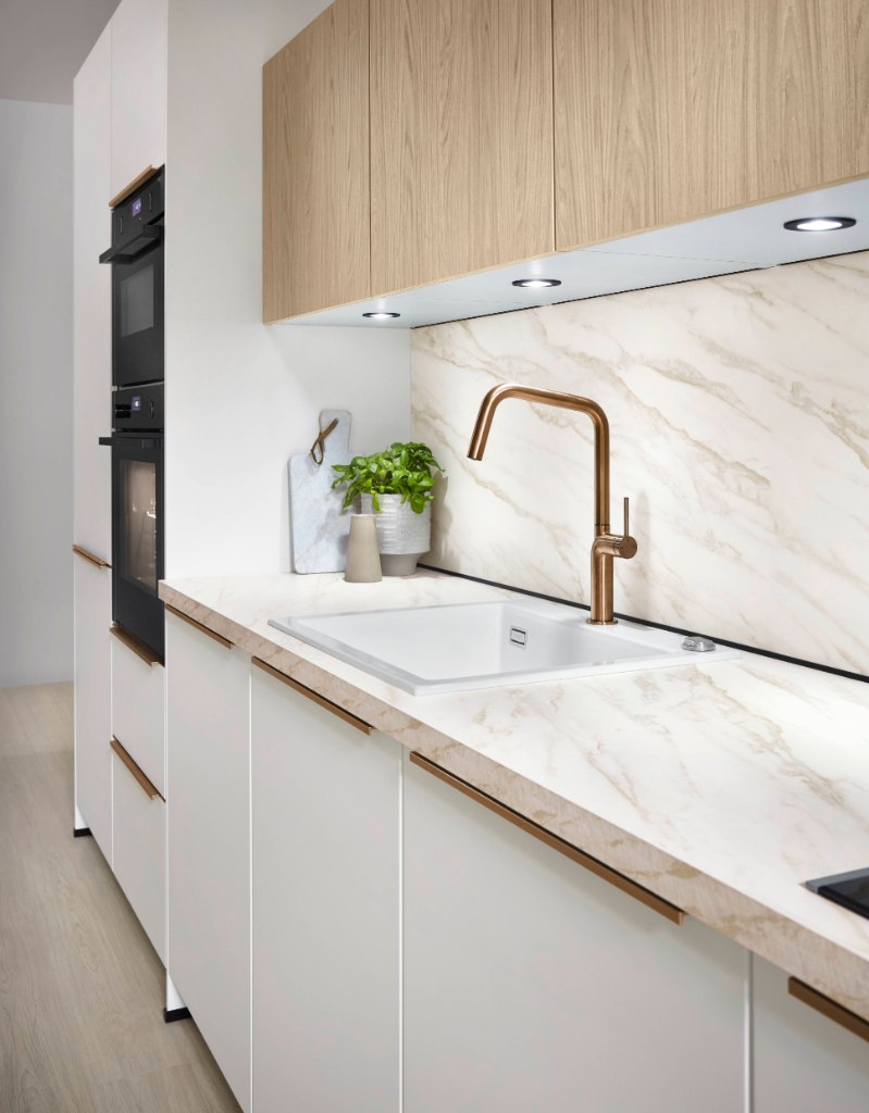 Cocina blanca con salpicadero de mármol, grifo dorado e iluminación bajo los muebles