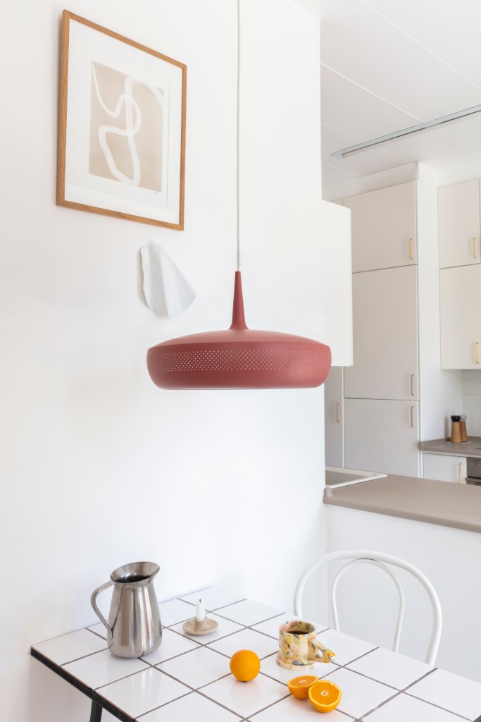 Lámpara colgante color teja sobre una mesa blanca con jarra y limones