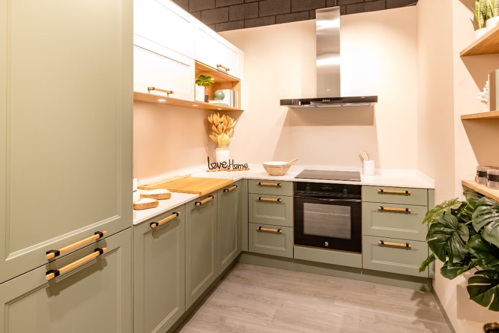 Cocina verde en esquina con encimera clara y tiradores dorados