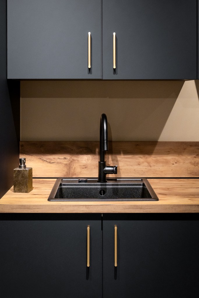 Fregadero negro integrado en encimera de madera con muebles azul noche y tiradores dorados