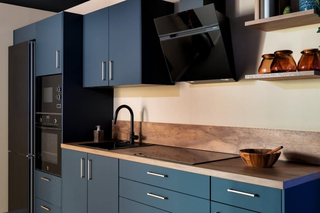 Cocina azul con encimera y salpicadero de madera, estante abierto y campana negra