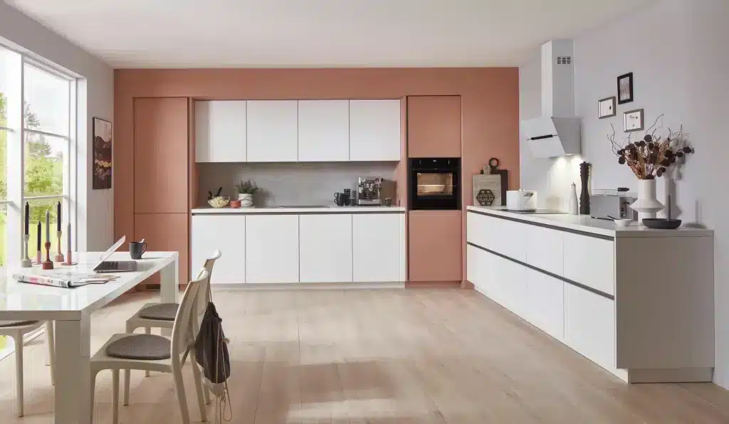 Cocina blanca en L con horno en columna y pared rosada
